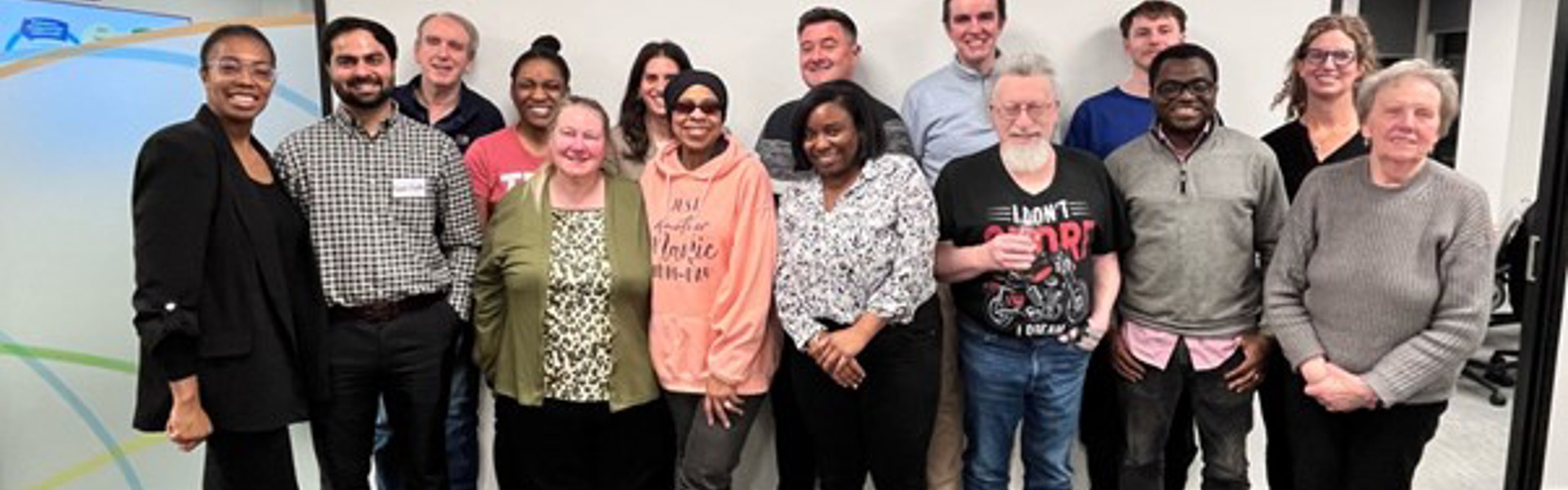 Group photo of the Resident Forum at NHG’s office. In the front row, seated left to right: Emma-Louise (resident Board member and Chair of the Resident Forum), Kautuk, Susan, Lin, Lacey, David, Ebenezer, and Mary. In the back row, standing left to right: Ian, Chioma, Rebecca, Robert, Gareth, Conrad, and Symmie (resident Board member). The group is smiling and facing the camera in a bright, modern meeting space, reflecting a collaborative and resident-led environment