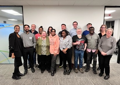 Group photo of the Resident Forum at NHG’s office. In the front row, seated left to right: Emma-Louise (resident Board member and Chair of the Resident Forum), Kautuk, Susan, Lin, Lacey, David, Ebenezer, and Mary. In the back row, standing left to right: Ian, Chioma, Rebecca, Robert, Gareth, Conrad, and Symmie (resident Board member). The group is smiling and facing the camera in a bright, modern meeting space, reflecting a collaborative and resident-led environment
