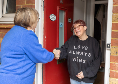 A smiling resident at the door to their home welcoming a housing officer. 