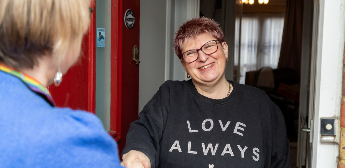 A smiling resident at the door to their home welcoming a housing officer.