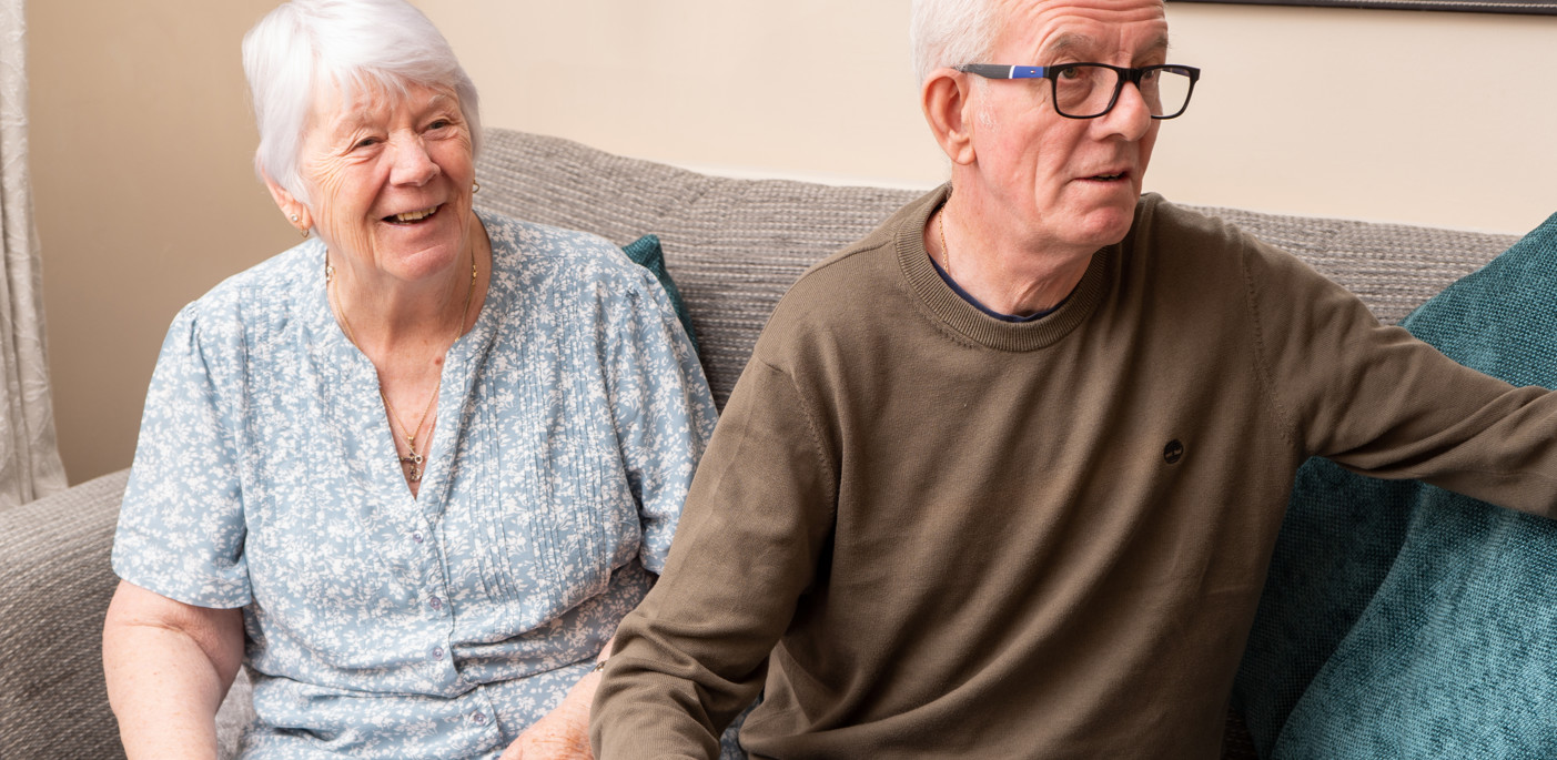 Two residents in their home seated on their sofa.